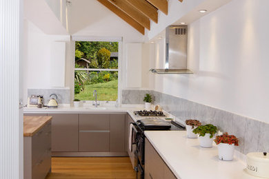 Medium sized contemporary l-shaped open plan kitchen in Other with an island, an integrated sink, flat-panel cabinets, beige cabinets, composite countertops, grey splashback, marble splashback, black appliances, medium hardwood flooring, brown floors, white worktops and exposed beams.