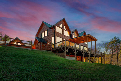 Large mountain style red two-story wood exterior home photo in Other with a metal roof and a black roof