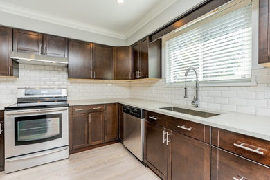 This is an example of a mid-sized transitional l-shaped open plan kitchen in Vancouver with an undermount sink, shaker cabinets, dark wood cabinets, quartz benchtops, white splashback, subway tile splashback, stainless steel appliances, light hardwood floors, with island, beige floor and white benchtop.