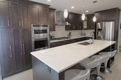 Example of a mid-sized trendy l-shaped light wood floor and yellow floor kitchen pantry design in Other with an island, an undermount sink, shaker cabinets, dark wood cabinets, quartz countertops, white backsplash, stone slab backsplash, stainless steel appliances and white countertops