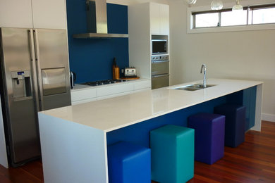 This is an example of a mid-sized contemporary galley eat-in kitchen in Wollongong with flat-panel cabinets, white cabinets, with island, an undermount sink, quartz benchtops, blue splashback, stainless steel appliances and medium hardwood floors.