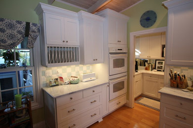 Inspiration for a large timeless l-shaped medium tone wood floor and beige floor eat-in kitchen remodel in Miami with white cabinets, granite countertops, white backsplash, white appliances, no island, an undermount sink, shaker cabinets and ceramic backsplash
