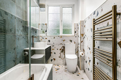 Inspiration for a small modern bathroom in London with black cabinets, a built-in bath, a shower/bath combination, a one-piece toilet, blue tiles, ceramic tiles, white walls, ceramic flooring, a wall-mounted sink, engineered stone worktops, multi-coloured floors, white worktops, a single sink and a floating vanity unit.