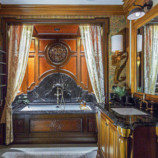 Удачное сочетание для дизайна помещения: ванная комната в классическом стиле с фасадами цвета дерева среднего тона, полновстраиваемой ванной, душем над ванной, мраморной плиткой, коричневыми стенами, врезной раковиной, мраморной столешницей, белым полом, шторкой для душа, черной столешницей и фасадами с выступающей филенкой - самое интересное для вас