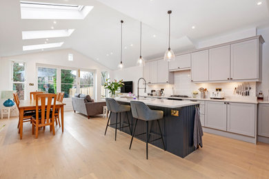 Inspiration for a large modern open plan kitchen in London with laminate floors, brown floors, a built-in sink, grey cabinets, an island, white worktops and feature lighting.