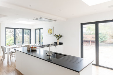 Example of a large danish l-shaped light wood floor and beige floor eat-in kitchen design in London with an undermount sink, flat-panel cabinets, white cabinets, quartzite countertops, a peninsula and black countertops