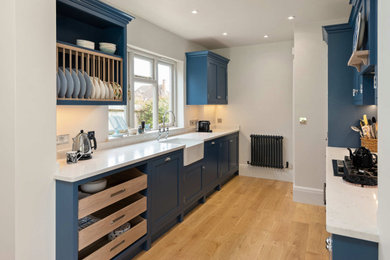 This is an example of a medium sized traditional open plan kitchen in Oxfordshire with a belfast sink, shaker cabinets, blue cabinets, quartz worktops, integrated appliances, an island and white worktops.