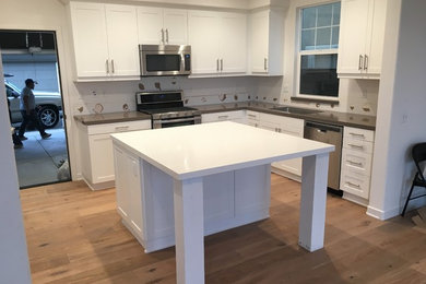 Design ideas for a small modern u-shaped eat-in kitchen in San Diego with a single-bowl sink, recessed-panel cabinets, white cabinets, granite benchtops, stainless steel appliances, light hardwood floors and with island.