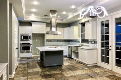 Large trendy l-shaped slate floor and multicolored floor eat-in kitchen photo in Houston with a double-bowl sink, recessed-panel cabinets, white cabinets, wood countertops, white backsplash, glass tile backsplash, stainless steel appliances, an island and white countertops