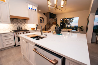 Example of a transitional l-shaped porcelain tile and gray floor eat-in kitchen design in Austin with an undermount sink, raised-panel cabinets, white cabinets, quartz countertops, white backsplash, marble backsplash, white appliances, an island and white countertops