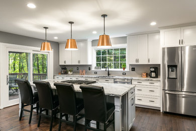 This is an example of a mid-sized transitional galley open plan kitchen in DC Metro with an undermount sink, shaker cabinets, white cabinets, granite benchtops, grey splashback, porcelain splashback, stainless steel appliances, with island, brown floor, dark hardwood floors and grey benchtop.