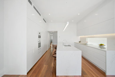 Design ideas for a beach style kitchen in Sydney with white cabinets, quartz benchtops, white splashback, medium hardwood floors, with island and white benchtop.