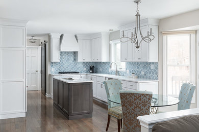 This is an example of a mid-sized transitional u-shaped eat-in kitchen in Chicago with an undermount sink, recessed-panel cabinets, white cabinets, quartz benchtops, blue splashback, ceramic splashback, stainless steel appliances, dark hardwood floors, with island, brown floor and white benchtop.