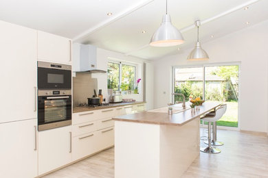 Idée de décoration pour une grande cuisine américaine parallèle et encastrable design avec un évier 1 bac, un placard à porte plane, des portes de placard blanches, îlot, un plan de travail en stratifié, une crédence grise, une crédence en dalle métallique, un sol en carrelage de céramique, un sol marron et un plan de travail marron.