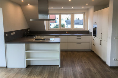 Moderne Küche mit flächenbündigen Schrankfronten, weißen Schränken, Arbeitsplatte aus Holz, Küchenrückwand in Schwarz, Halbinsel und schwarzer Arbeitsplatte in Leipzig