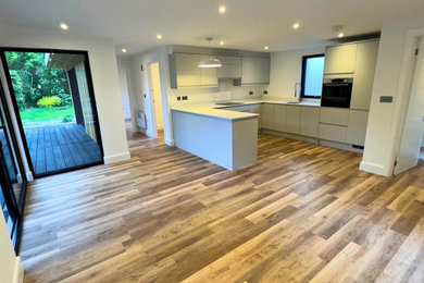 Modern l-shaped open plan kitchen in Surrey with laminate floors, an island and white worktops.