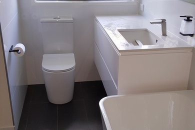 This is an example of a large contemporary wet room bathroom in Brisbane with white cabinets, a freestanding tub, a wall-mount toilet, white tile, white walls, cement tiles, an undermount sink, engineered quartz benchtops and an open shower.