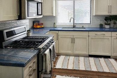 Small beach style u-shaped dark wood floor and brown floor enclosed kitchen photo in San Luis Obispo with a single-bowl sink, shaker cabinets, white cabinets, granite countertops, white backsplash, subway tile backsplash, stainless steel appliances and blue countertops