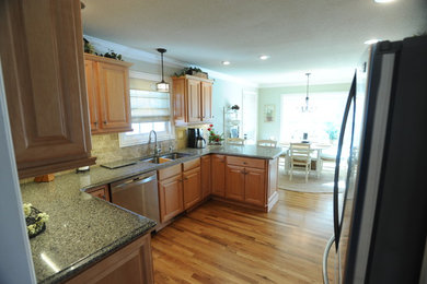 Inspiration for a mid-sized timeless u-shaped light wood floor eat-in kitchen remodel in Other with an undermount sink, raised-panel cabinets, light wood cabinets, granite countertops, beige backsplash, stone tile backsplash, stainless steel appliances and a peninsula