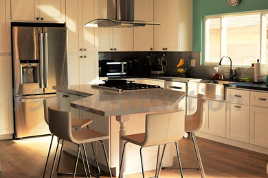 Eat-in kitchen - mid-sized modern u-shaped light wood floor eat-in kitchen idea in San Diego with a farmhouse sink, raised-panel cabinets, white cabinets, granite countertops, gray backsplash, ceramic backsplash, stainless steel appliances and an island