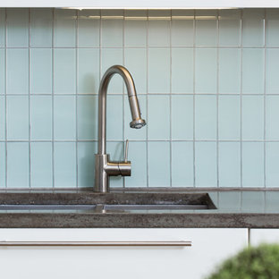 Inredning av ett retro stort kök, med en undermonterad diskho, släta luckor, vita skåp, bänkskiva i betong, blått stänkskydd, stänkskydd i glaskakel, rostfria vitvaror, mellanmörkt trägolv och en köksö