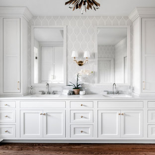 Example of a large classic master white tile and porcelain tile medium tone wood floor, brown floor, double-sink, tray ceiling and wallpaper bathroom design in Nashville with recessed-panel cabinets, white cabinets, a two-piece toilet, gray walls, an undermount sink, quartz countertops, a hinged shower door, white countertops, a niche and a built-in vanity