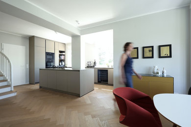 Offene Moderne grifflose Küche mit Unterbauwaschbecken, flächenbündigen Schrankfronten, beigen Schränken, Quarzwerkstein-Arbeitsplatte, schwarzen Elektrogeräten, hellem Holzboden, Kücheninsel, beigem Boden und beiger Arbeitsplatte in Frankfurt am Main