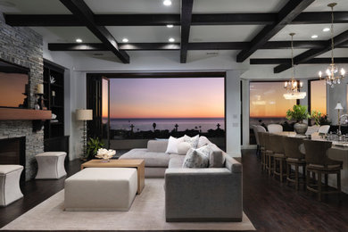 Living room - huge coastal open concept dark wood floor, brown floor and coffered ceiling living room idea in San Luis Obispo with gray walls, a standard fireplace, a stacked stone fireplace and a wall-mounted tv