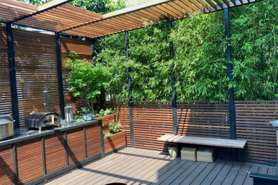 Large minimalist backyard ground level metal railing outdoor kitchen deck photo in New York with a pergola