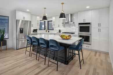 Example of a mid-sized farmhouse l-shaped light wood floor and brown floor eat-in kitchen design in Edmonton with a farmhouse sink, shaker cabinets, white cabinets, quartz countertops, white backsplash, ceramic backsplash, stainless steel appliances, an island and white countertops