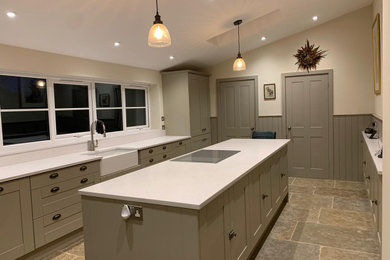 Photo of a medium sized traditional galley enclosed kitchen with a belfast sink, shaker cabinets, grey cabinets, composite countertops, white splashback, an island and white worktops.