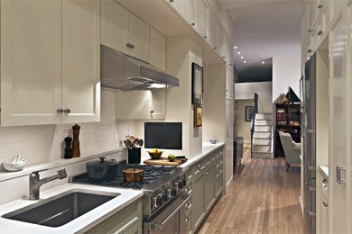 Photo of a mid-sized traditional galley kitchen in New York with an undermount sink, shaker cabinets, white cabinets, quartz benchtops, white splashback, ceramic splashback, stainless steel appliances and medium hardwood floors.