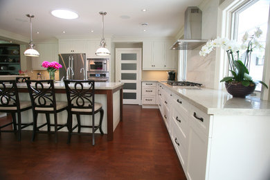 Large transitional l-shaped eat-in kitchen in Toronto with an undermount sink, shaker cabinets, white cabinets, stainless steel appliances, dark hardwood floors, with island and brown floor.