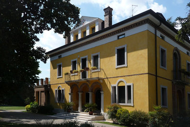 Diseño de fachada de casa amarilla campestre grande de tres plantas con revestimientos combinados, tejado a doble faldón y tejado de teja de barro
