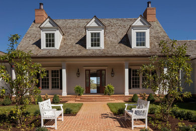 Cette photo montre une grande façade de maison blanche chic à un étage avec un toit mixte et un toit marron.