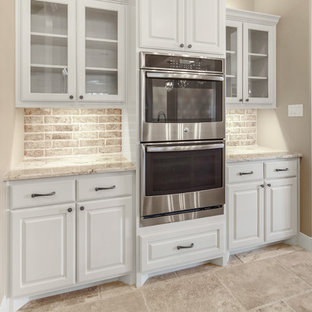 Idéer för att renovera ett stort medelhavsstil skafferi, med en rustik diskho, luckor med upphöjd panel, beige skåp, granitbänkskiva, beige stänkskydd, stänkskydd i tegel, rostfria vitvaror, travertin golv, en köksö och beiget golv