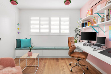 Imagen de despacho moderno pequeño con paredes rosas, suelo de madera clara y escritorio empotrado