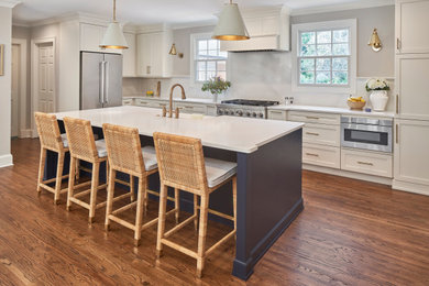 Inspiration for a large coastal l-shaped medium tone wood floor and brown floor eat-in kitchen remodel in Charlotte with a farmhouse sink, shaker cabinets, white cabinets, quartz countertops, white backsplash, quartz backsplash, stainless steel appliances, an island and white countertops