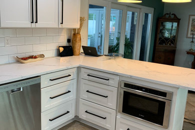 タンパにある広いモダンスタイルのおしゃれなキッチン (ドロップインシンク、シェーカースタイル扉のキャビネット、白いキャビネット、クオーツストーンカウンター、白いキッチンパネル、サブウェイタイルのキッチンパネル、シルバーの調理設備、セラミックタイルの床、ベージュの床、白いキッチンカウンター) の写真