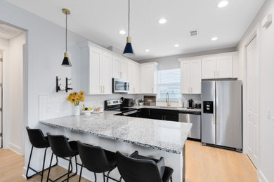 Trendy l-shaped eat-in kitchen photo in Orlando with white cabinets, granite countertops, white backsplash and multicolored countertops