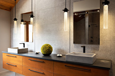 Large contemporary master bathroom in Other with flat-panel cabinets, medium wood cabinets, a double shower, a one-piece toilet, gray tile, grey walls, a vessel sink, grey floor, a hinged shower door, black benchtops, concrete floors and concrete benchtops.