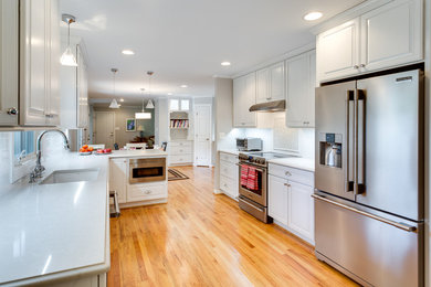 Example of a large transitional medium tone wood floor kitchen design in Baltimore with an undermount sink, raised-panel cabinets, white cabinets, quartz countertops, stainless steel appliances and a peninsula