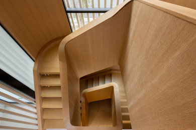 Example of a large minimalist spiral wood railing and wood wall staircase design in Los Angeles with wooden risers