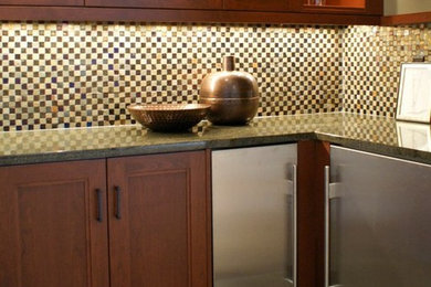 Inspiration for a transitional l-shaped porcelain tile wet bar remodel in Cleveland with an undermount sink, recessed-panel cabinets, medium tone wood cabinets, granite countertops, multicolored backsplash and mosaic tile backsplash