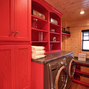 Imagen de cuarto de lavado lineal, rural, de tamaño medio, con armarios con paneles lisos, puertas de armario rojas, encimera de laminado, paredes marrones, suelo de madera en tonos medios y lavadora y secadora juntas