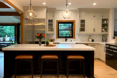 Trendy light wood floor and brown floor kitchen photo in Milwaukee with a farmhouse sink, recessed-panel cabinets, white cabinets, quartzite countertops, white backsplash, an island and white countertops