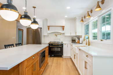 Mid-sized farmhouse l-shaped laminate floor and brown floor kitchen pantry photo in Newark with a farmhouse sink, shaker cabinets, white cabinets, quartzite countertops, white backsplash, subway tile backsplash, stainless steel appliances, an island and white countertops