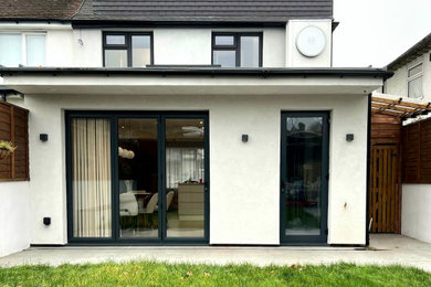 This is an example of a white modern render and rear house exterior in London with three floors, a flat roof, a tiled roof and a black roof.