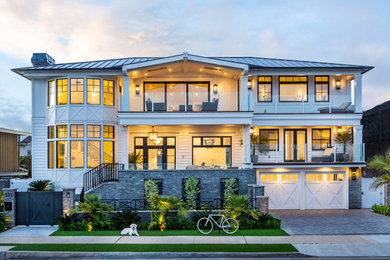 Inspiration for a large coastal white two-story board and batten house exterior remodel in San Diego with a hip roof, a metal roof and a gray roof