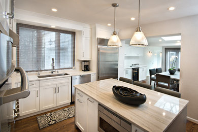 This is an example of a mid-sized transitional l-shaped eat-in kitchen in Chicago with shaker cabinets, white cabinets, with island, an undermount sink, quartz benchtops, white splashback, stainless steel appliances, dark hardwood floors, brown floor and white benchtop.